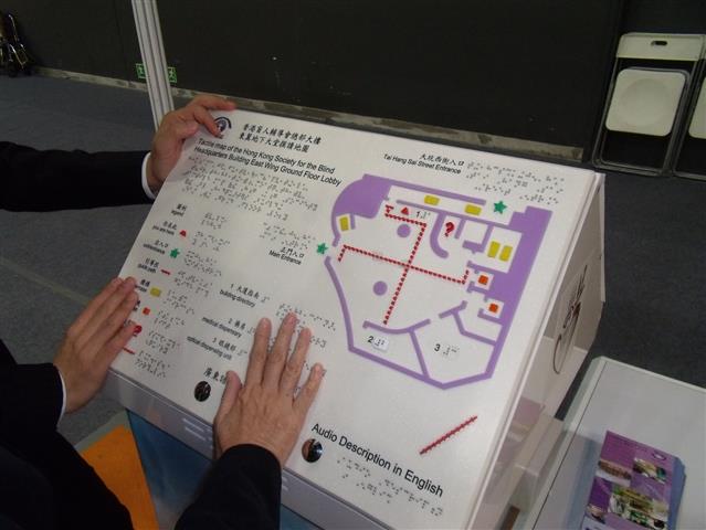 A tactile directory and map located on an inclined podium featuring braille and tactile lettering. The map incorporates colour and shape coding to identify key elements and routes. The directory also provides audio information through the push of a button.