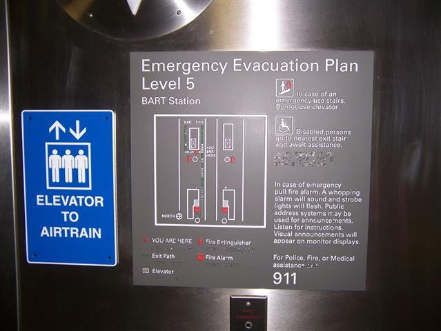 A tactile emergency evacuation plan sign. Information is presented visually and through tactile elements including a map, raised lettering, pictograms and braille. 